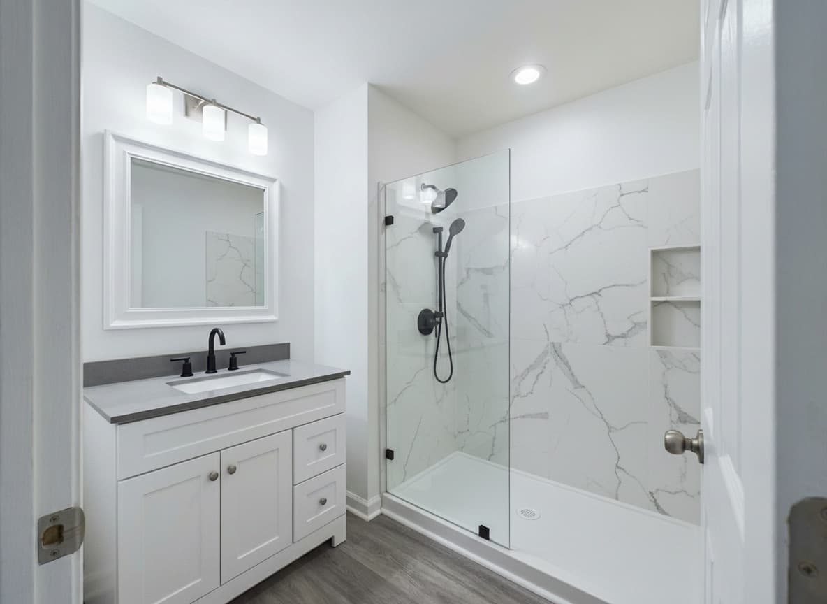 Modern SwanStone walk-in shower with Carrara marble panels, glass panel, matte black fixtures, and white shaker vanity